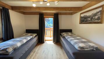 A room with two beds, wooden beams on the ceiling, a painting on the wall, and a balcony with a view.