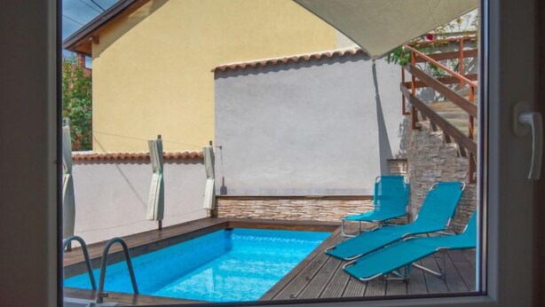A view of a swimming pool with lounge chairs and a wooden deck, visible through a window. - Vacation home Veli by Interhome (Opatija/Veli Brgud)
