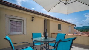A patio with a round table and four chairs, an umbrella, and a view of the mountains. - Vacation home Veli by Interhome (Opatija/Veli Brgud)