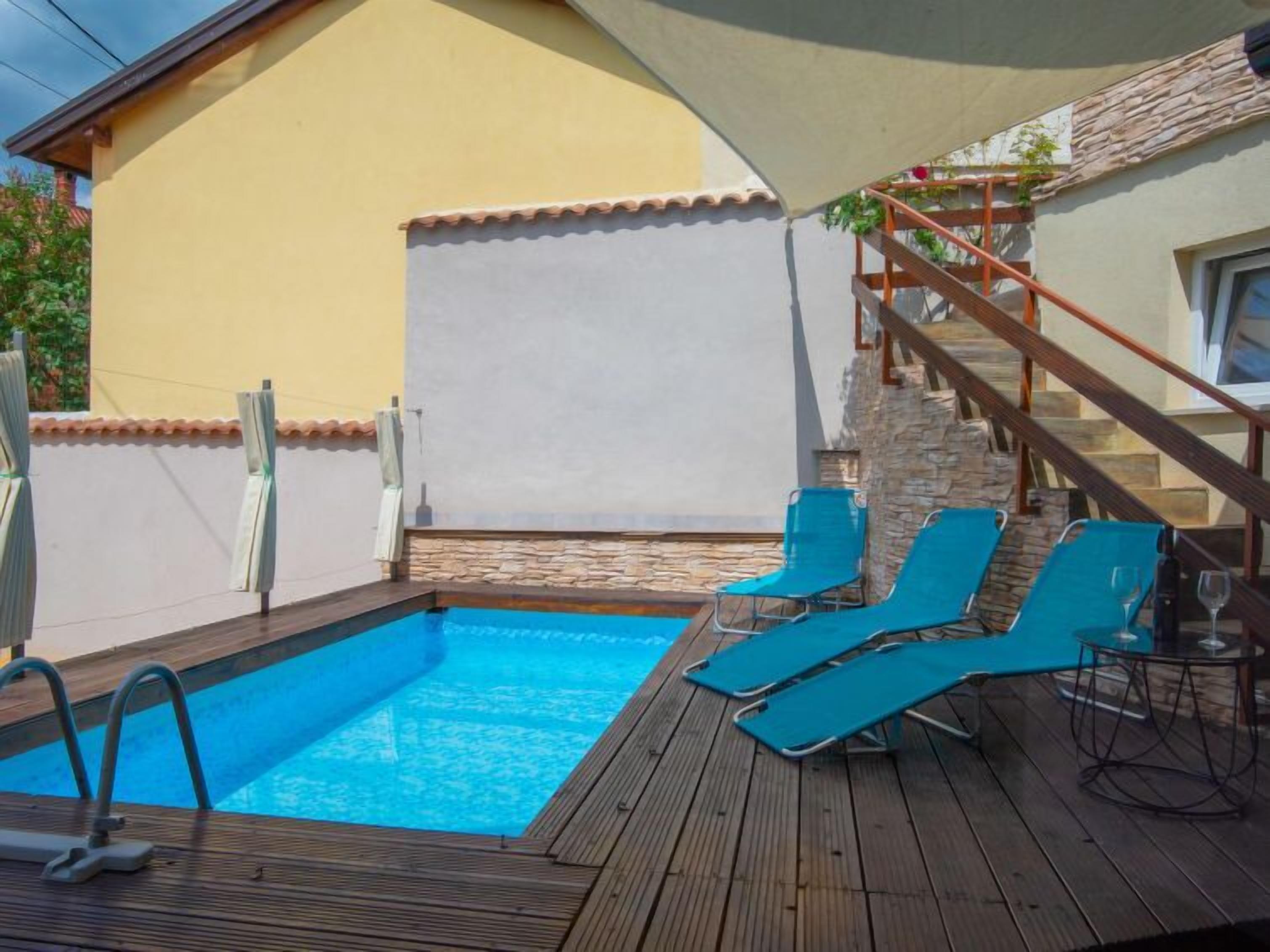 Una terrassa de fusta amb una piscina, gandules blaves i una escala que mena a una paret de pedra.