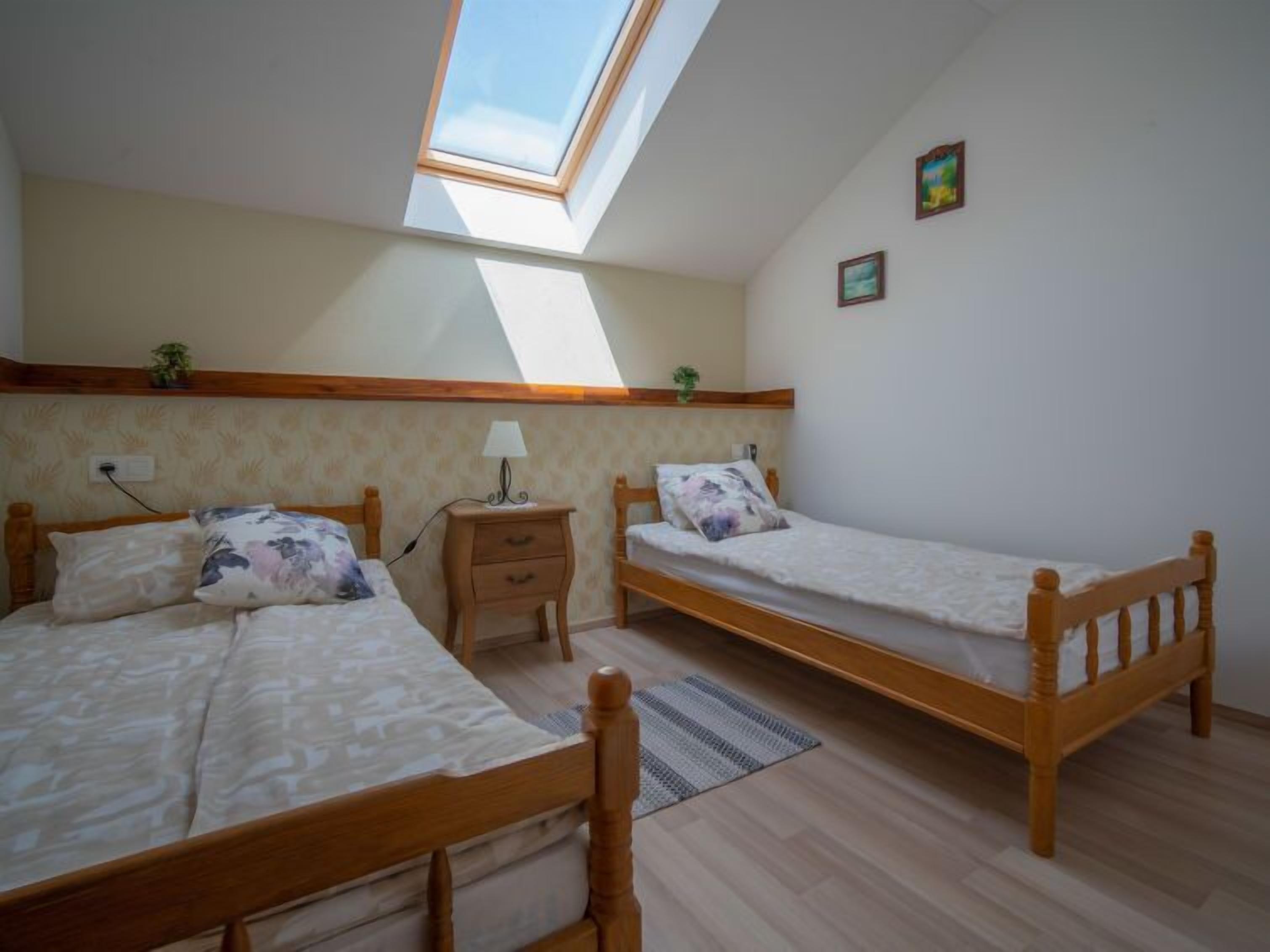 Ein Zimmer mit zwei Holzbetten, einem Oberlicht, einem kleinen Nachttisch mit Lampe und einer Wandsteckdose.