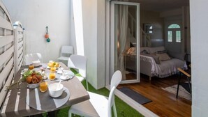 Zona pranzo con tavolo apparecchiato per la colazione, una porta scorrevole in vetro che dà su una camera da letto e un muro esterno bianco.