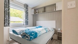 Un dormitorio con cama, ventana con cortinas, radiador y estanterías empotradas con objetos decorativos.