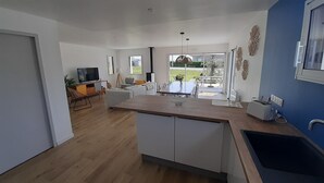 Une cuisine moderne dotée d’un îlot central, d’un coin repas avec une table et des chaises, et offrant une vue sur l’extérieur grâce à de grandes fenêtres.