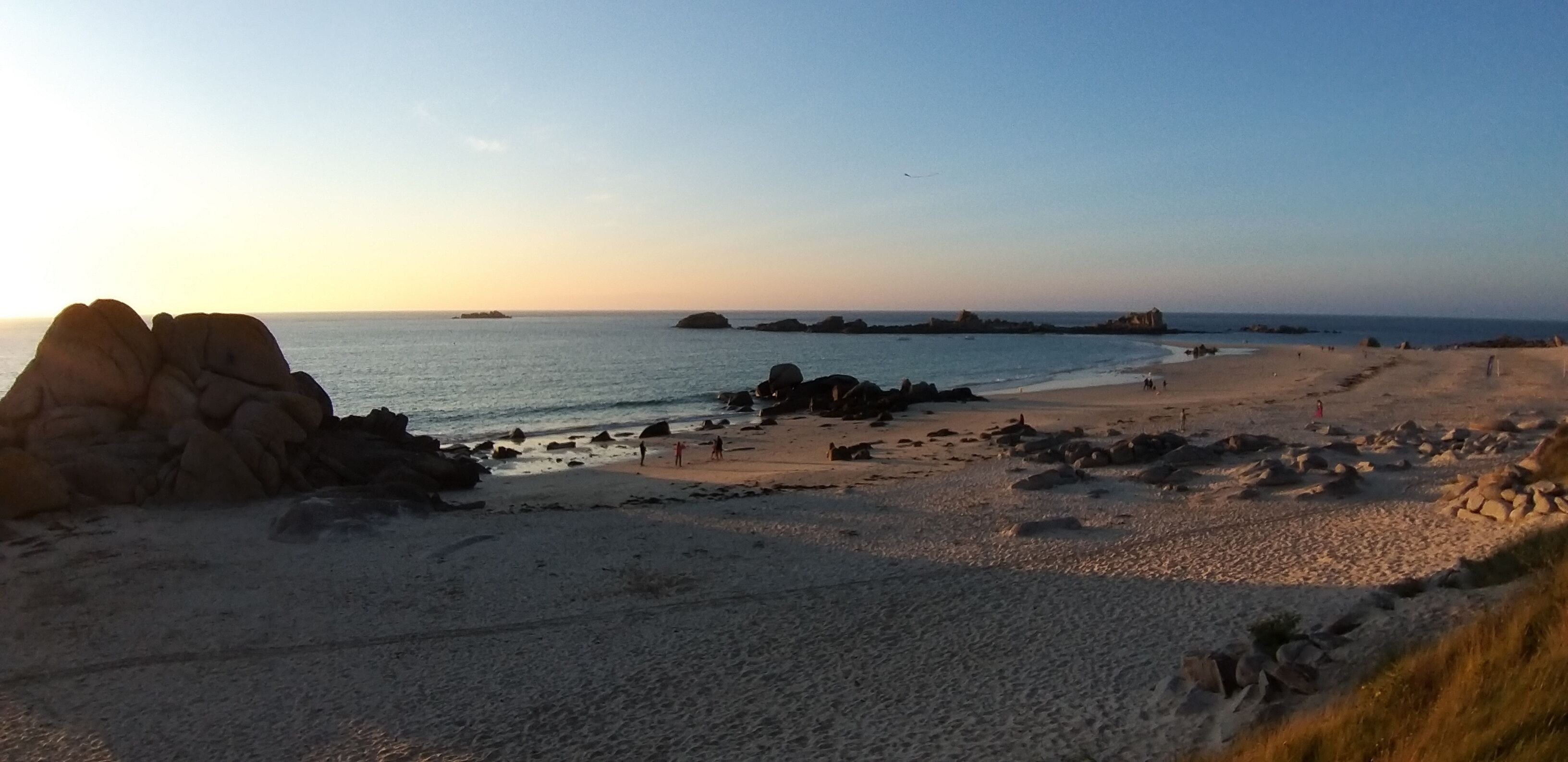 A beach with rocky formations, calm water, and a clear sky.