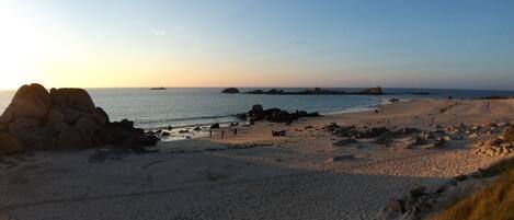 A beach with rocky formations, calm water, and a clear sky.
