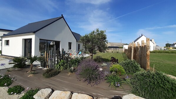 A modern house with a large glass door, surrounded by a well-maintained garden with various plants and a wooden deck.