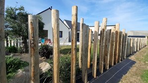 Une rangée de poteaux en bois dans un jardin, avec une maison et des panneaux solaires en arrière-plan.