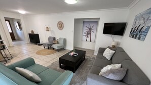 A living room with a teal sofa, a grey sofa, a coffee table, and a TV mounted on the wall. - Sandstone Point (SEQ) Bribie Holidays Family Home, pet friendly  (Sandstone Point)