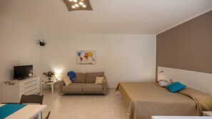 A modern hotel room with a bed, a sofa, a TV, and a desk.