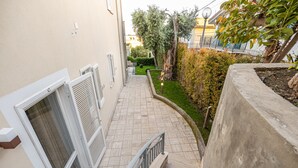 A narrow outdoor corridor with a concrete wall on one side and a building entrance on the other.