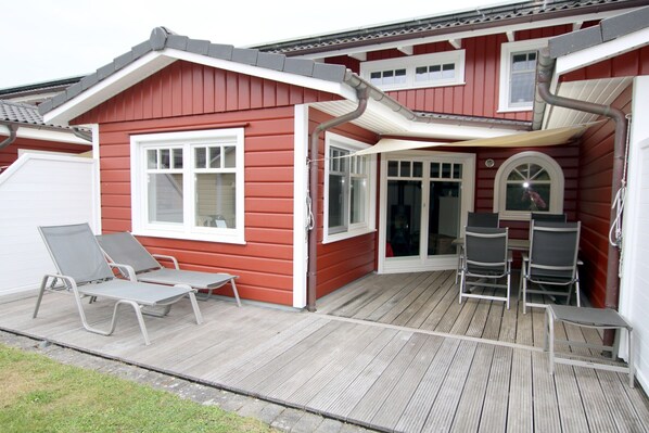 Uma casa vermelha com deck de madeira, duas cadeiras de descanso e uma mesa.