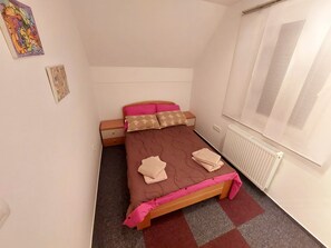 Quarto pequeno e bem arrumado, com uma cama de solteiro, uma mesa de cabeceira e um radiador.