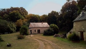 A rustic stone building with a dirt path leading to it, surrounded by trees and greenery.