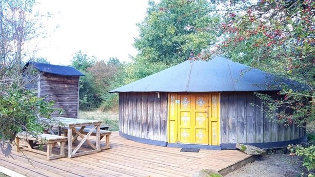 A wooden cabin with a yellow door, a wooden deck, and a small table.