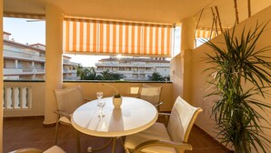 A balcony with a round table, chairs, a potted plant, and a view of buildings. - LA MARINA LM075 (Denia)