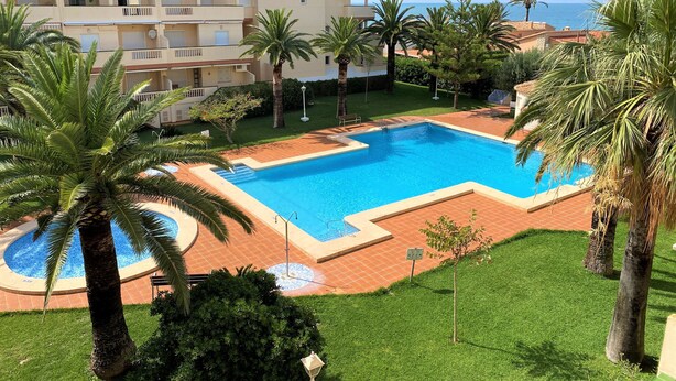A swimming pool surrounded by palm trees and a building with balconies. - LA MARINA LM075 (Denia)