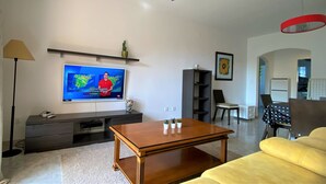 A living room with a TV, sofa, coffee table, and a dining area with chairs. - LA MARINA LM075 (Denia)