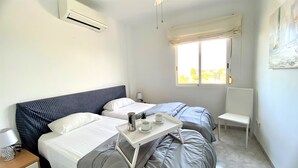 A hotel room with two beds, a small table with a tray of items, a chair, and a window with a view. - LA MARINA LM075 (Denia)