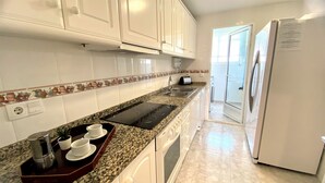 A kitchen with white cabinets, a granite countertop, a built-in oven, a refrigerator, and a window with a view. - LA MARINA LM075 (Denia)