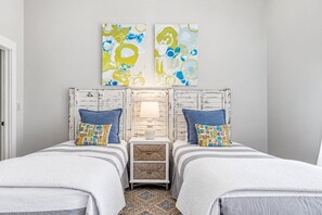 A bedroom with two beds, a nightstand, a lamp, and abstract wall art.