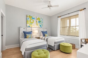 A bedroom with two beds, a ceiling fan, a window with curtains, and a view of the outdoors.
