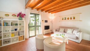 A living room with a white sofa, two armchairs, a coffee table, a TV, a bookshelf, and a window with curtains.