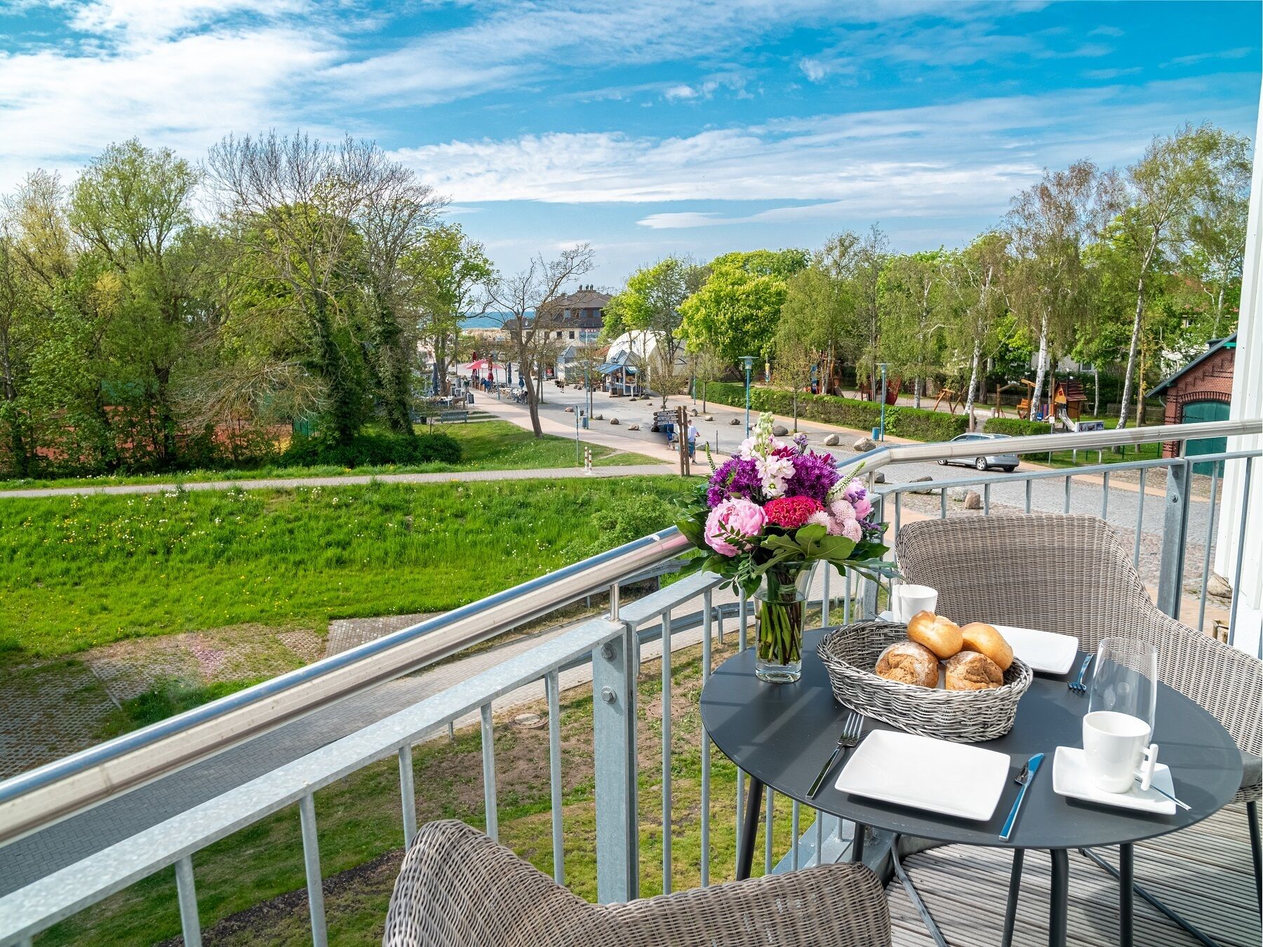 A balcony with wicker furniture, a table with a vase of flowers, and a basket of bread.