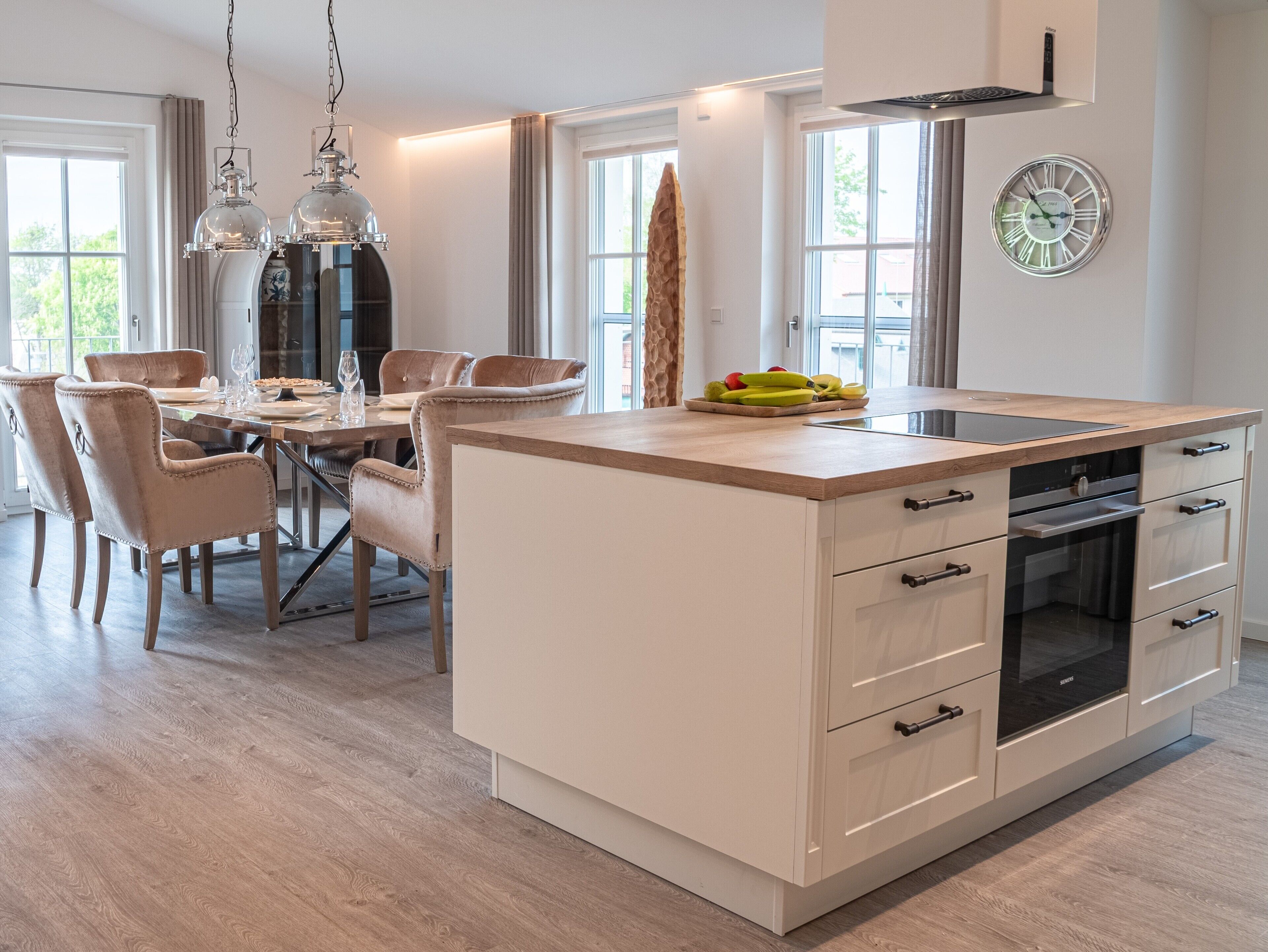 A modern kitchen with a central island, a dining area with chairs, and a large window providing natural light.