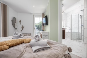 Ein Hotelzimmer mit Bett, Fernseher, Badezimmer mit Dusche und Balkon mit Aussicht.
