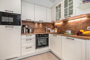 Cozinha moderna com armários brancos, forno embutido, cafeteira e painel de madeira.