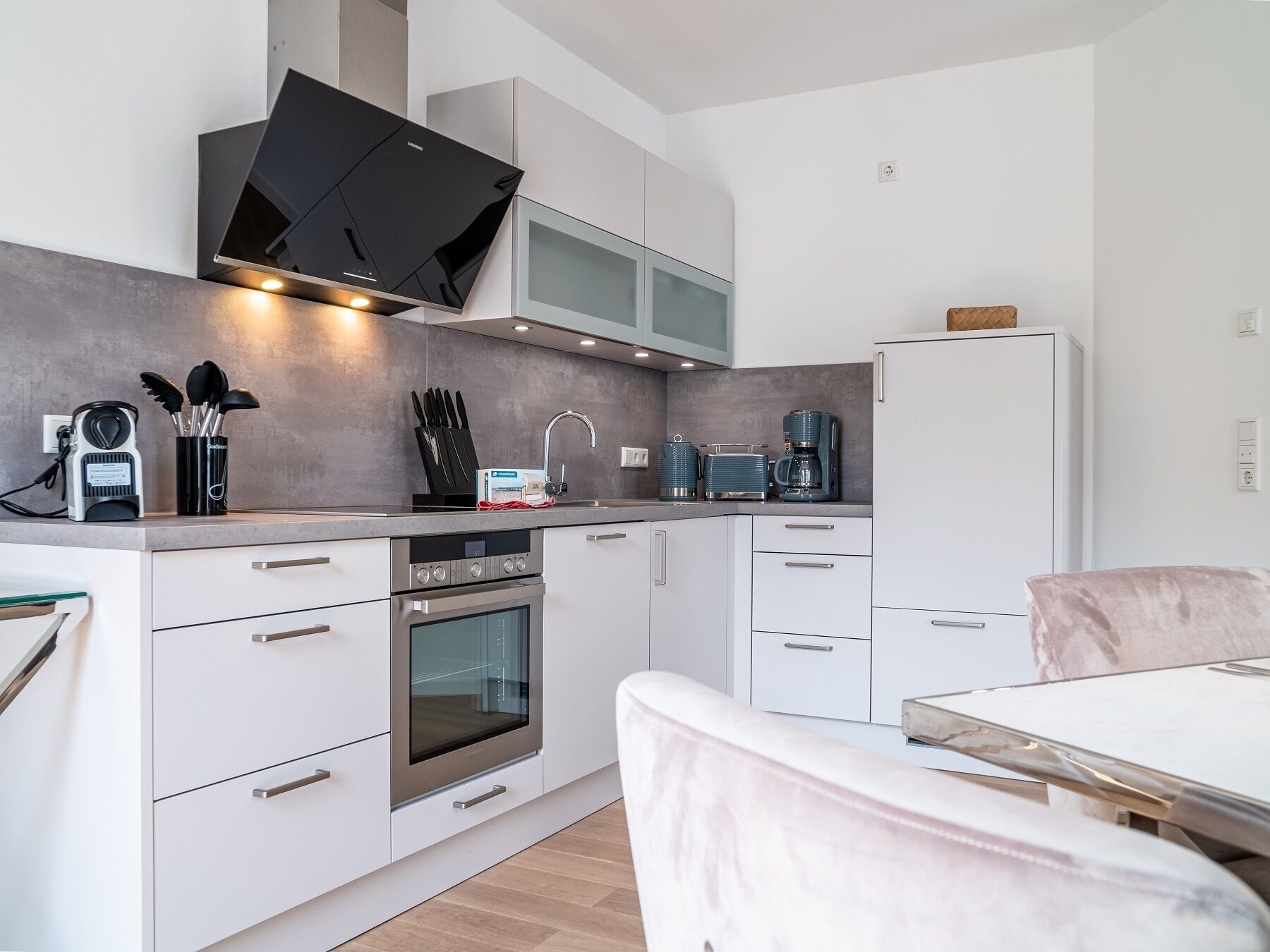 A modern kitchen with white cabinets, a built-in oven, a microwave, and a coffee maker.
