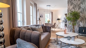 A modern living room with a brown sofa, a round coffee table, and a dining area in the background. - Obergeschosswohnung Panorama-residenz 26 (Ostseebad Wustrow)