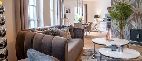 A modern living room with a brown sofa, a round coffee table, and a dining area in the background.
