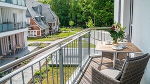 A balcony with wicker furniture and a table, overlooking a garden and neighboring buildings. - Obergeschosswohnung Panorama-residenz 26 (Ostseebad Wustrow)