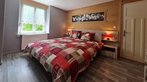 Un dormitorio con una cama grande, una ventana con cortinas, cabecera de madera, un cuadro en la pared y una puerta.