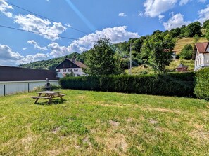 A grassy area with a picnic table, a white building with a dark roof, and a body of water in the background. - Cozy 85m² Apartment, Near Ski Trails & Nature, Fully Equipped, Parking, WiFi, Sleeps 8 (La Bresse)