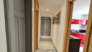 Un pasillo estrecho con estructura y suelo de madera que conduce a una cocina con armarios rojos.