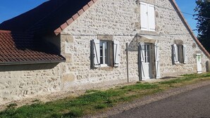 A stone building with a sloped roof, a door, and windows with shutters.