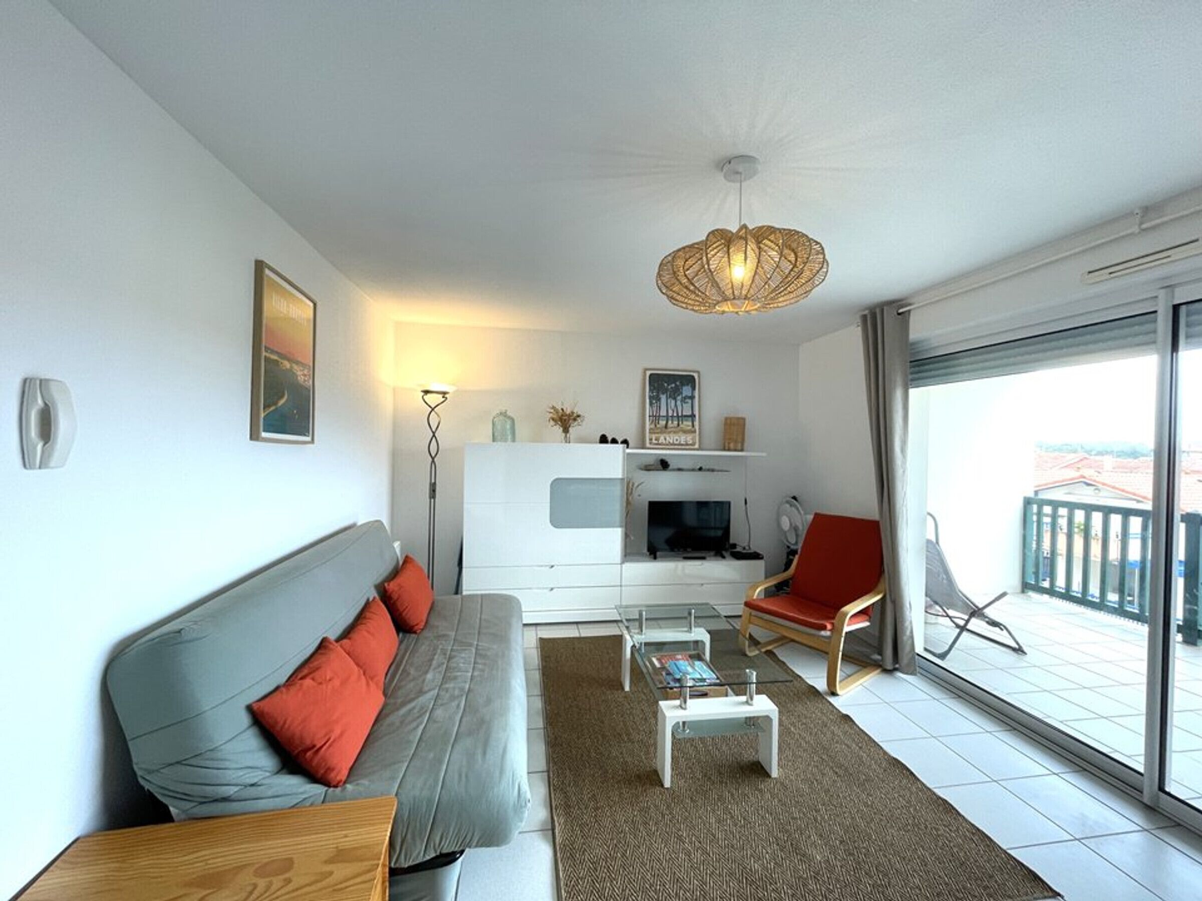 Ein modernes Wohnzimmer mit einer Couch, einem Couchtisch und einem roten Sessel. Ein Fernseher und eine Lampe stehen auf einem weißen Schrank.