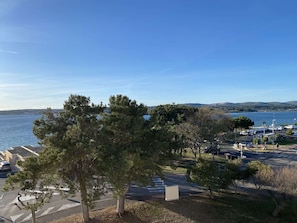 Un parking ombragé par des arbres, avec vue sur un plan d’eau.