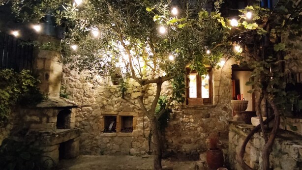 Une cour pavée de pierres, avec des murs en pierre rustique, une petite fenêtre et des lampes suspendues.