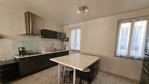 A modern kitchen with dark cabinets, a white countertop, a stainless steel range hood, and a coffee maker. There is a window with white curtains and a small bar area with stools. - Townhouse in Orléans, near Loire and center (Orléans)