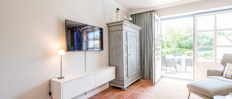 A modern living room with a flat-screen TV mounted on the wall, a grey cabinet, a white console table, and a beige sofa.