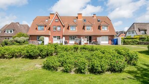 A large brick house with a red-tiled roof, multiple windows, and a well-maintained garden in front.