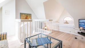 A modern loft bedroom with a sloped ceiling, a white bed, a TV, and a glass table with a magazine.