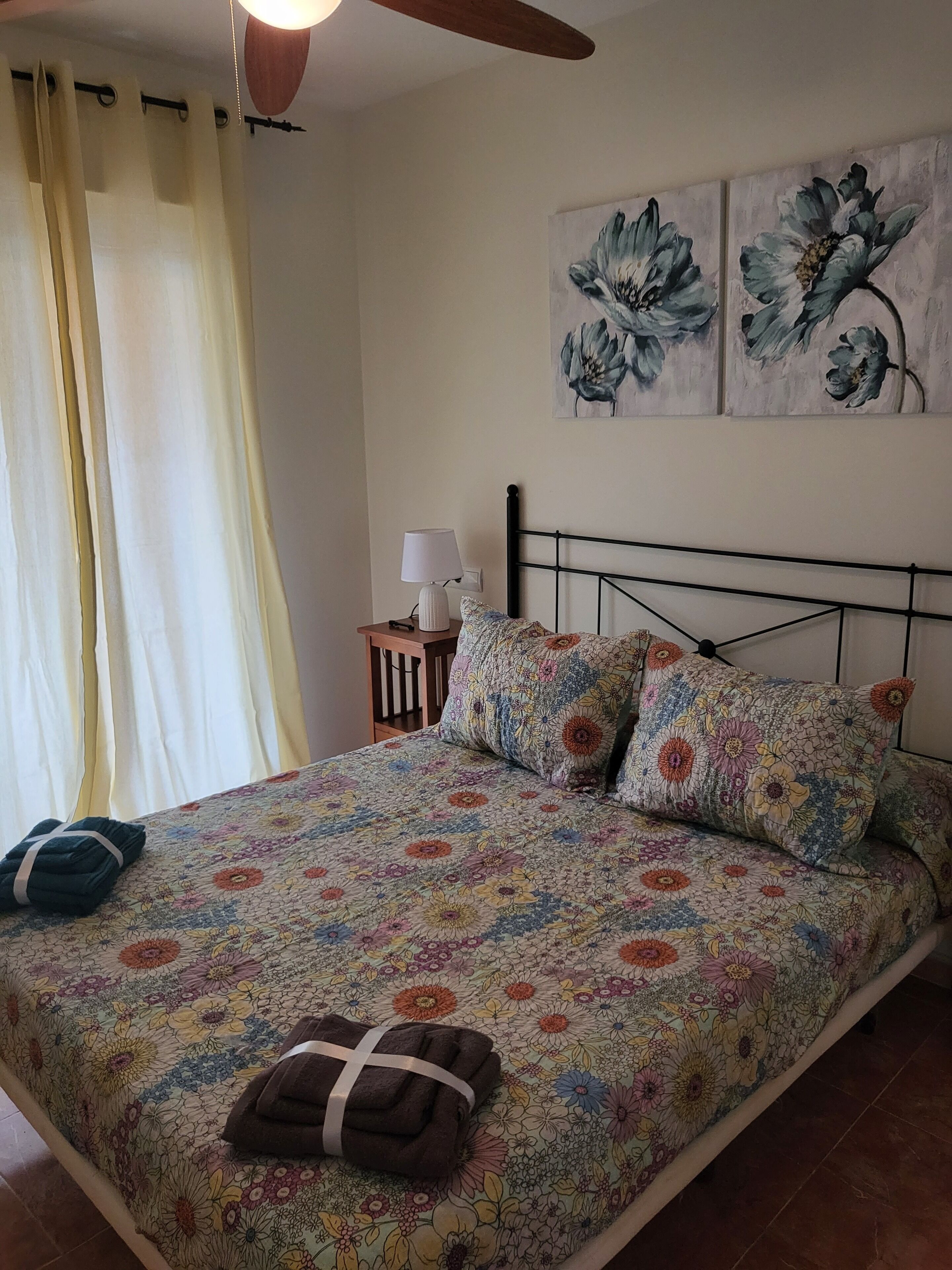 Ein ordentlich bezogenes Bett mit Blumenmuster, eine Nachttischlampe und ein Kopfteil mit geometrischem Design.