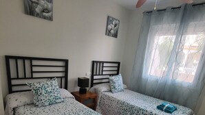 Ett hotellrum med två sängar, en takfläkt och ett fönster med gardiner.