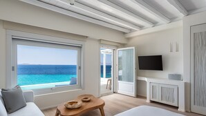 A modern hotel room with a large window overlooking the sea, a bed, a wooden table, and a television. - Villa Santa Esmeralda Mykonos (Mykonos)