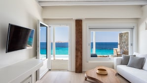 A modern living room with a TV, a wooden coffee table, a white sofa, and a view of the ocean. - Villa Santa Esmeralda Mykonos (Mykonos)